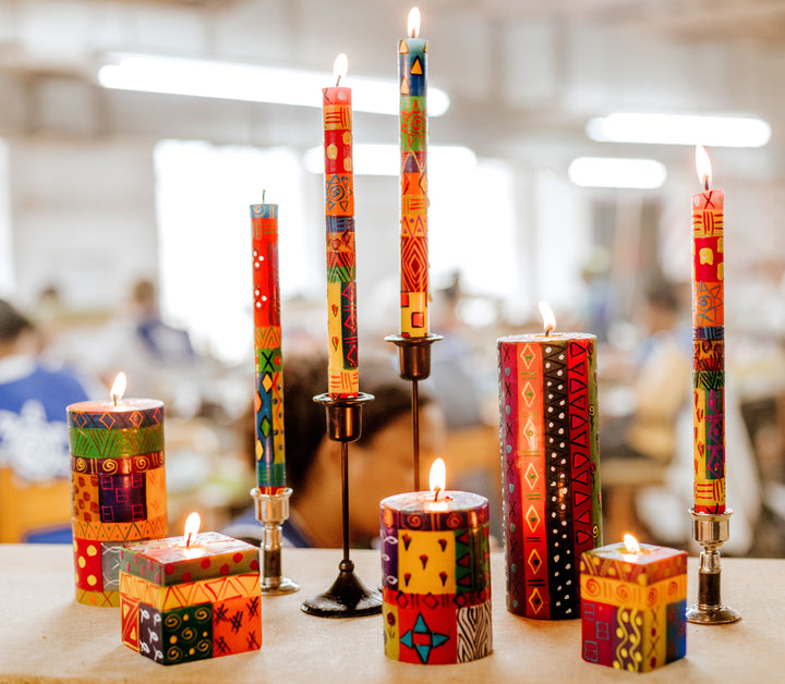 Lifestyle photo of Multicolor Ethnic collection all burning brightly with the artisan painting candle in the background.