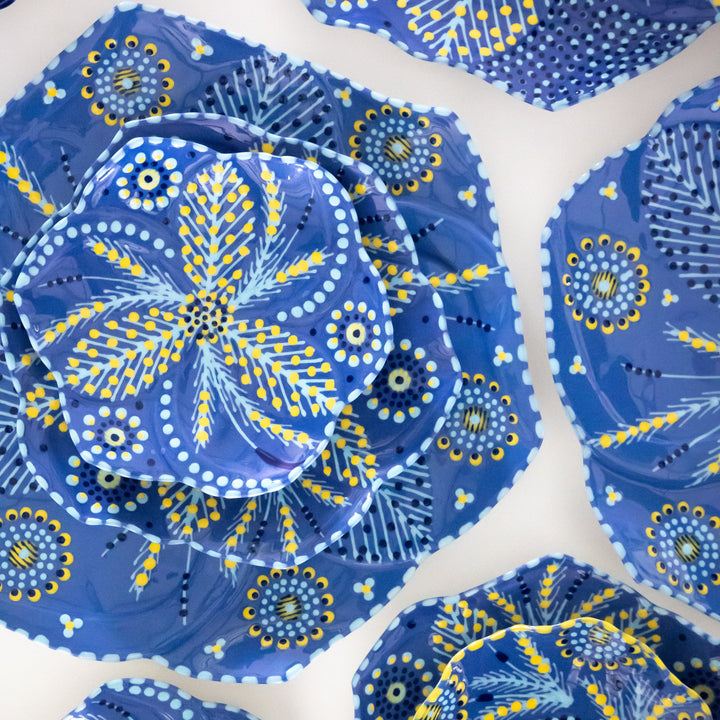 Tulip cocktail plate on sine plate on dinner plate with indigo blue background, baby blue and yellow floral design.  This is a sample of the other colors available for the ceramic dinner set.