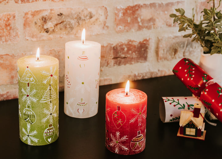 Lifestyle photo of Whimsy Christmas pillars! 3x6 white, 3x6& green and 3x4 red all lite with delicate 'whimsy' Christmas designs of snowflake, ornament, & tree.