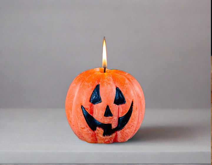 Whimsy Pumpkin candle! Orange with a Jack o' Lantern face painted on in black.  This pumpkin is lit sitting on a wooden table with a black background - BOO!