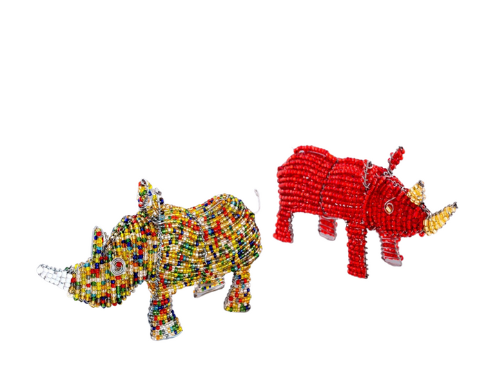 Two beaded rhino figurines made of recycled silver wire and a mix of opaque and transparent beads. The rhino on the left is multicolor with mostly yellow beads and many pops of red, orange, green, blue, and opaque white beads as the horn. The rhino on the right is solid transparent red beads with the horns and eyes a yellow gold bead.