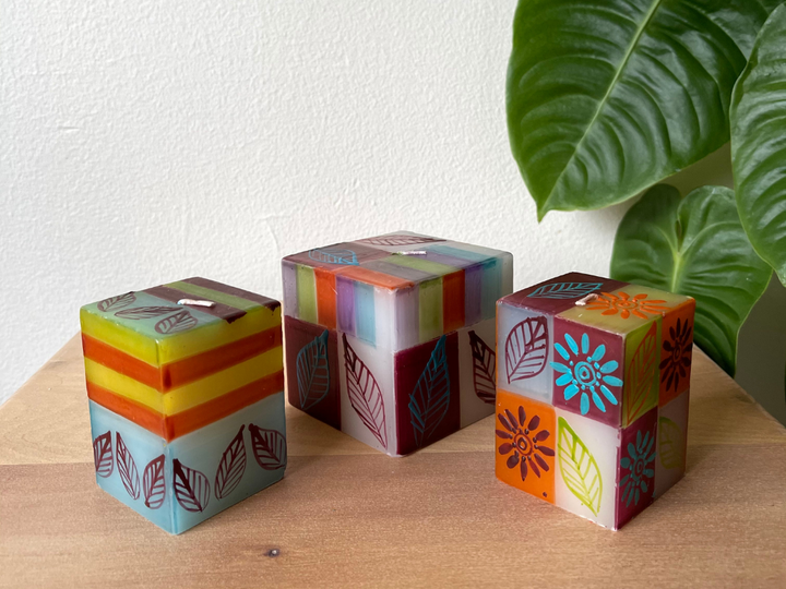 Magic Garden cube candles.  Two 2" x 2" x 3"  and one 3" x 3" x 3" cube candle.  Striped and square backgrounds of muted garden colors with floral pattern overlays. Fair Trade product.